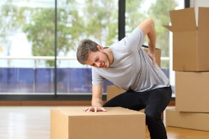 young man with packing boxes grabbing back in pain