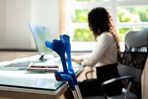 young woman with crutches doing office work