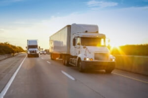 Two semi-trucks on highway with trailing passenger car