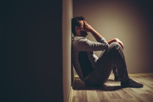 young man sitting in dark room on the floor, covering his face